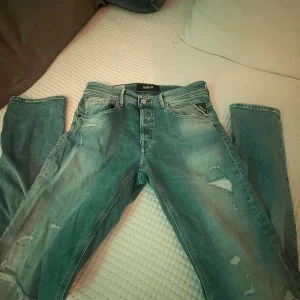 Replay ljusblå slitna jeans - Säljer ett par ljusblå jeans från Replay med slitna detaljer och snygga revor på benen. Klassisk femficksmodell med knapp och dragkedja framtill. Jeansen har en smal passform och är tillverkade i mjukt denimtyg.