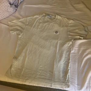 Vit t-shirt från Stone Island - Säljer en clean vit t-shirt från Stone Island med klassisk logopatch på bröstet. T-shirten har rund hals och korta ärmar, perfekt för dig som gillar stilrena plagg med premiumkänsla. Materialet är mjuk bomull för skön komfort. T-shirten är äkta och använd ett fåtal gånger.