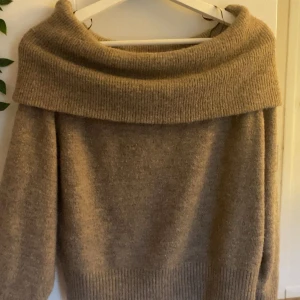 Beige stickad offshoulder tröja H&M - Supermysig beige stickad tröja från H&M i offshoulder-modell. Tröjan har bred ribbad kant upptill som ger en chill och snygg look. Perfekt för dig som gillar neutrala färger och vill ha något extra till garderoben.