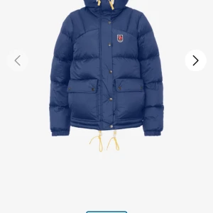 Blå dunjacka från Fjällräven - Säljer en blå dunjacka från Fjällräven med huva och gula snören. Jackan har två stora fickor med knappar, dragkedja och tryckknappar framtill samt Fjällrävens klassiska logga på bröstet. Perfekt för kalla dagar och har en riktigt puffig look. Använd fåtal gånger och köpte helt ny💕