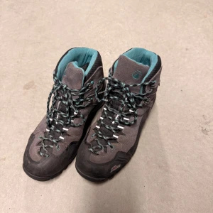 Grå och turkosa kängor från Uppi - Säljer ett par grå kängor från Uppi med turkosa detaljer och snörning. Skorna har robust platt sula och är tillverkade i syntet och mocka, perfekta för utomhusaktiviteter. Insidan är mjukt vadderad för extra komfort och de har rund tå.