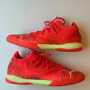 Röda Puma inomhusfotbollsskor 40.5 - Säljer ett par grymma röda Puma inomhusfotbollsskor med limegröna detaljer och snörning. Skorna har stickad ovandel och platt sula med bra grepp, perfekt för snabba vändningar på planen. Snygg design med små mönstrade detaljer och Puma-logga på sidan och sulan.