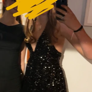 Svart glittrig kortklänning med djup v-ringning - Supersnygg svart kortklänning med massor av glittrande paljetter och djup v-ringning. Klänningen är ärmlös och har öppen rygg, perfekt för dig som vill sticka ut. Sitter tajt upptill och har en lätt utsvängd kjol.