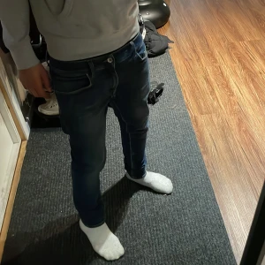 Blå Tiger of sweden jeans slim fit 31/32 - Säljer ett par snygga blå Tiger of sweden jeans med slim fit och klassisk femficksdesign. Jeansen har en mörk tvätt med lätt slitning, bruna detaljer vid linningen och smal passform som sitter tajt vid benen. Perfekt för dig som gillar stilrena och moderna jeans.