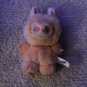 Pop Mart The Monsters Plush - Söt och unik Pop Mart The Monsters-mjukis i rosa päls med karaktäristiskt ansikte. Märkt med originaletiketter från Pop Mart och The Monsters. Mycket fint skick, inga synliga defekter eller slitage. Perfekt för samlare eller som present.