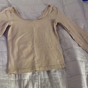 Beige långärmad topp från H&M Divided - Säljer en beige långärmad topp från H&M Divided i storlek XS. Toppen har en djup rundad halsringning och är tillverkad i mjukt, stretchigt material som sitter skönt mot kroppen. Perfekt för att styla med jeans eller kjol för en enkel och snygg look.