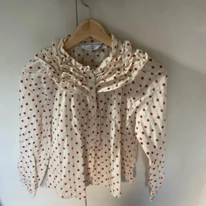  blus med volang från other stories  - Supersöt vit blus från other stories med små jordgubbar. Blusen har volang vid kragen och knappar framtill.