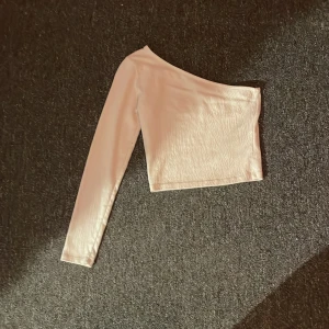 Vit oneshoulder topp från H&M - Säljer en vit croppad topp från H&M med oneshoulder-design och lång ärm. Toppen är tillverkad i ett lätt, strukturerat material som ger en cool känsla. Perfekt för dig som vill sticka ut med en enkel men snygg look.