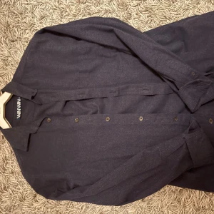 Mörkblå skjorta från Minimum, S - Snygg mörkblå skjorta från Minimum i storlek S. Skjortan har klassisk krage, knappar hela vägen och långa ärmar med manschett. Materialet känns mjukt och är troligtvis bomull, perfekt för en clean och stilren look.