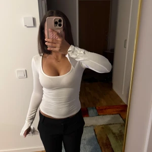 Gina Tricot vit långärmad topp - Säljer en vit långärmad topp från Gina Tricot i stretchigt bomullsmaterial. Toppen har en djup rundad urringning och sitter tight mot kroppen för en snygg siluett. Perfekt att styla med jeans eller kjol för en clean look. Knappt använd!