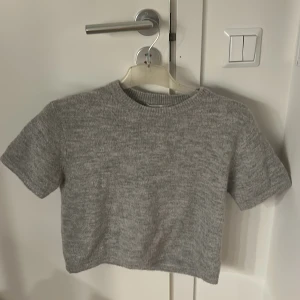Grå stickad topp - Säljer en grå stickad topp med korta ärmar och rund hals. STORLEK 146/152, men passar mig som är S, den är bara lite över byxhöjd. 