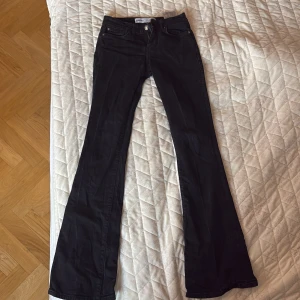 Svarta bootcut jeans från Bershka - Svarta jeans från Bershka i bootcut-modell med klassisk femficksdesign och dragkedja. Snygg passform med utsvängda ben och midja som sitter bekvämt. Perfekta för dig som gillar en stilren och trendig look.