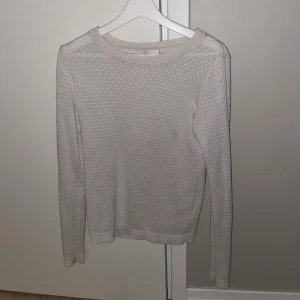 Vit stickad tröja med strukturmönster - Säljer en vit stickad tröja med snyggt strukturmönster och rund hals. Tröjan har långa ärmar och ribbade muddar vid ärmslut och nederkant. Perfekt för dig som gillar stilrena och enkla plagg med lite extra detalj.