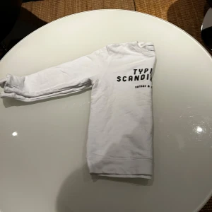 Vit sweatshirt från Samsøe & Samsøe - Vit sweatshirt med trycket 'Typical Scandinavian' från Samsøe & Samsøe. Tröjan har rund hals, långa ärmar och en klassisk passform. Mjuk och skön bomullskvalitet som passar perfekt till jeans eller joggers. Enkel och stilren design med svart text framtill.