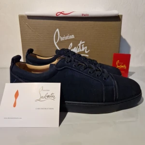 Mörkblå sneakers från Christian Louboutin 43 - Snygga mörkblå sneakers från Christian Louboutin med klassisk röd sula och broderad logga på hälen. Skorna har rund tå, snörning och är tillverkade i mocka med läderdetaljer på insidan. Perfekt för dig som vill sticka ut med exklusiv stil.