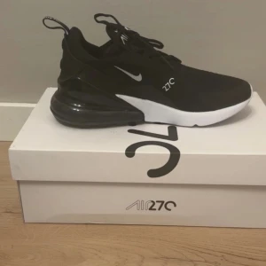 Nike Air Max 270 svart/vit strl 38 - Nike Air Max 270 sneakers i svart och vitt med stor synlig Air-enhet i hälen. Ovandel i mesh och syntet, klassisk Nike Swoosh på sidan och 270-logga. Skon har snörning och en chunky, sportig vibe. Perfekt för dig som gillar streetstyle och bekväma sneakers. Oanvända helt nya