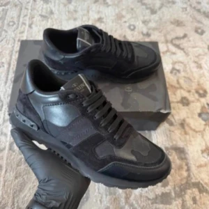 Valentino Rockrunner svarta sneakers - Svarta Valentino Rockrunner sneakers med snygga camouflagemönster och detaljer i både skinn och mocka. Klassisk rund tå, platt sula och snörning. Perfekta för dig som gillar exklusiva och stilrena sneakers med edge.