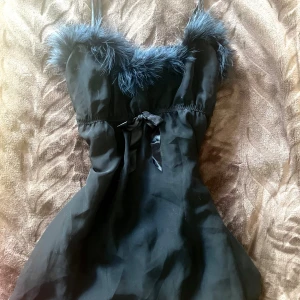 Svart topp linne med pälsdetalj - Supersnygg svart topp  med fluffig pälsdetalj längs urringningen och tunna axelband. söt rosett framtill i midjan och är perfekt för dig som vill sticka ut. Materialet känns lätt och har en fin fallande form.