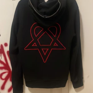 HIM hoodie  - Svart hoodie från ANCY med stor röd heartagram-tryck på ryggen och dragkedja framtill. Tröjan har huva, fickor och ribbade muddar. Perfekt för dig som gillar streetstyle och vill sticka ut med en unik detalj på ryggen. Passar som stor S är mer M, köpt från Vinted aldrig använt sen dess. Tunn och har dragkedja på luvan o priset kan alltid diskuteras 