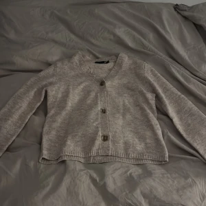 Beige kofta från 157, XS - Mysig beige kofta från 157 i storlek XS. Koftan har v-ringning, tre knappar framtill och är långärmad. Materialet är stickat och ger en chill vibe, perfekt att slänga på sig när det är lite kyligt ute.