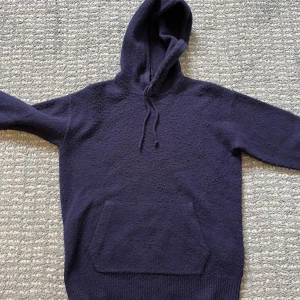 Polo Ralph Lauren Kashmirhoodie - Mörkblå hoodie från Polo Ralph Lauren med huva och snörning. Tröjan har en stor magficka och är stickad i en lyxig blandning av ull och kashmir. Perfekt för dig som gillar klassisk stil med premiumkänsla.