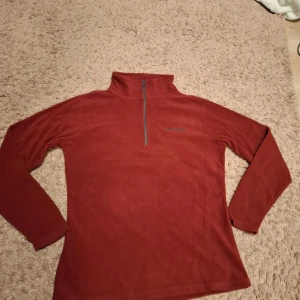 Röd fleece-tröja från Stormberg - Mysig röd fleece-tröja från Stormberg med hög krage och half zip framtill. Perfekt för kyliga dagar och outdoor-aktiviteter. Långärmad och i mjukt fleecematerial som håller dig varm och bekväm.