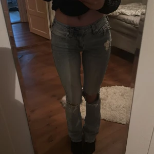 True Religion ljusblå bootcut jeans - Säljer ett par ljusblå jeans från True Religion med slitningar och hål vid knäna. Klassiska bakfickor med broderad logga och knappdetalj. Jeansen har bootcut-modell och låg midja, tillverkade i jeansmaterial. Perfekta för en avslappnad och trendig look. Skit snygga men lite för stora för mig i midjan ‼️ Användt 3 gånger, och super sköna 🥰