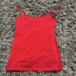 Röd linnetopp med smala axelband - En enkel och snygg röd linnetopp med smala axelband. Perfekt för varma dagar eller att styla lager på lager. Toppens material känns mjukt och lätt mot huden.