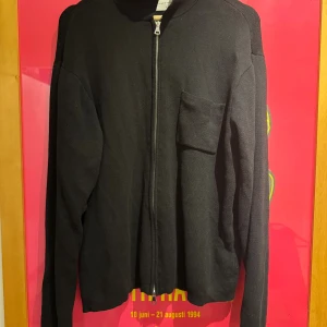 Svart stickad kofta från Studio Total - Svart stickad kofta från Studio Total i storlek M. Koftan har en rak passform, lång ärm och en praktisk bröstficka. Stängs med dragkedja framtill och är perfekt för lager-på-lager. Enkel och stilren design som funkar till många olika looks.