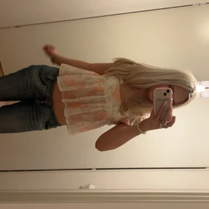 Blommig volangblus med puffärm - Supersöt blus med blommigt mönster i ljusa toner av beige, rosa och orange. Modellen är croppad med volanger vid axlarna och har en luftig, flowy passform. Blusen är ärmlös och har en fyrkantig halsringning. Perfekt för sommarens alla tillfällen!