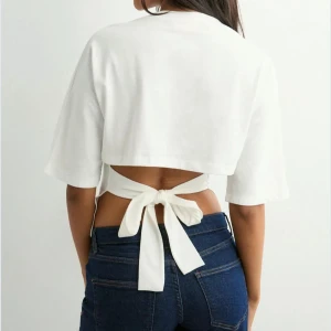 Open back tie tee från Nelly  - Säljer en vit croppad topp med breda korta ärmar och snygg knytning i ryggen. Toppen har en stilren design med öppen rygg och är tillverkad i mjuk bomull. Perfekt för dig som vill ha en enkel men ändå unik look.