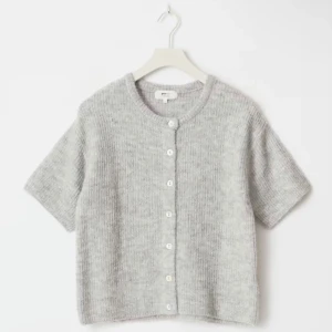 Grå stickad kofta med kort ärm - Supermysig grå kofta från Gina Tricot med stickad struktur och korta ärmar. Den har rund hals och vita knappar framtill som ger en clean look. Perfekt att styla med jeans eller kjol för en chill vibe.