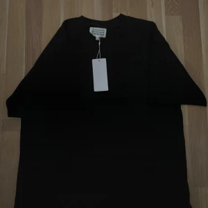 Maison Margiela svart t-shirt med print - Svart t-shirt från Maison Margiela med vit grafisk print och siffror på ryggen. Klassisk rund hals och korta ärmar. Materialet är mjuk bomull och passformen är normal. Snygg och stilren design med coola detaljer. pris kan diskuteras 