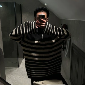 Randig stickad tröja med dragkedja - Säljer en mysig svart och beige randig stickad tröja med dragkedja i halsen. Tröjan har långa ärmar och en avslappnad passform, perfekt för kyliga dagar. Använd sparsamt, inga defekter över huvudtaget!! Lånade bilder, fick precis hem den men den var inget för mig 