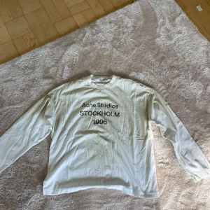 Vit långärmad tröja Acne Studios - Vit långärmad tröja från Acne Studios med svart tryck på bröstet där det står 'Acne Studios STOCKHOLM 1996'. Tröjan har rund halsringning och är gjord i mjuk bomull. Perfekt för en clean och stilren look. ny pris 3500