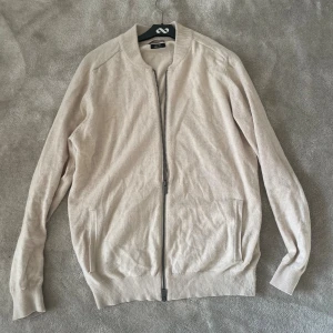 Beige kofta med dragkedja Massimo Dutti - Stilren beige kofta från Massimo Dutti i en mjuk merino ull. Modellen har lång ärm, ribbade muddar och hel dragkedja framtill. Perfekt för lager-på-lager och enkel att matcha med det mesta.