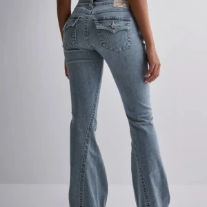 Ljusblå bootcut jeans true religion - Snygga ljusblå jeans med bootcut passform och markerade bakfickor med lock och dekorativa sömmar från true religion. Jeansen har klassisk femficksdesign, knapp och dragkedja framtill samt är tillverkade i jeansmaterial. Perfekta för dig som gillar en retroinspirerad look. Det enda är att de har slitningar längst ner. Pris diskuteras inte!!!!