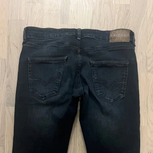 Svarta jeans från Guess med raka ben - Säljer ett par svarta jeans från Guess med klassisk femficksdesign och snygga detaljer på bakfickorna. Jeansen har raka ben och en mörk tvätt med diskreta slitningar. Guess-logga på bakfickan och läderpatch i midjan. Perfekta för dig som gillar stilrena jeans med en cool touch.