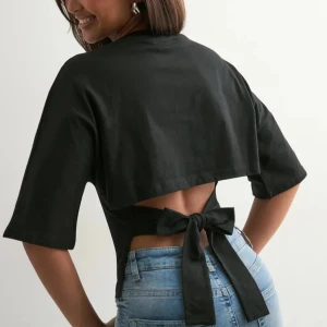 Svart topp med knyt i ryggen - Svart topp med halvlånga ärmar och rund halsringning. Baksidan har en öppen detalj med breda band som knyts i en stor rosett i midjan. Funkar för båda vardag pch lite festligare tillfällen🖤