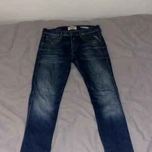Replay slim fit anbass Hyperflex blå jeans - Snygga Replay Hyperflex anbass jeans i klassisk blå tvätt med slitningar och snyggt faded effekt. Jeansen har raka ben, fem fickor och bruna detaljer i läder vid linningen. Stretchigt material som ger en skön passform och rörelsefrihet.