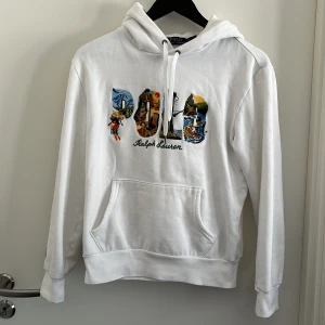 Ralph lauren hoodie  - Säljer en snygg vit hoodie från Ralph Lauren med färgglatt broderi på bröstet som bildar ordet 'POLO'. Tröjan har en klassisk justerbar huva. Perfekt för en stilren och bekväm look. Nypris runt 2500, mitt pris endast 545. Svår att få tag på, skicket är som ny 