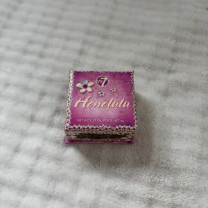 W7 Honolulu Bronzer med borste - Säljer en W7 Honolulu bronzer i en söt lila kartong med blommigt mönster. Kommer med en platt borste som passar perfekt för contouring. Bronzing-pudret ger en solkysst look och är lätt att applicera. Förpackningen är kompakt och smidig att ta med i väskan.