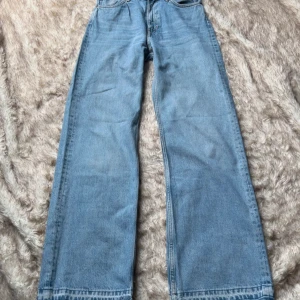 Ljusblå wide jeans från Monki - Blå jeans med vida ben. Fransade benslut. Knapp och dragkedja. 100% bomull. Storlek 27, motsvarar stl 36.  Midja tvärsöver 36 cm Innerbenslängd ca 81 cm