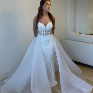 Brudklänning(ny) - Helt ny med etikett. Ångrade mitt köp av denna brudklänning med glittrande detaljer och pärlor. Klänningen har axelband med pärlor och en voluminös kjol. Den är dekorerad med pärlor och har en korsettliknande överdel som ger en smickrande passform. Ny pris 22.000kr.