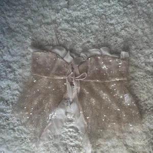 Glittrig rosa korsettopp från Zara - Supersöt korsettopp från Zara i ljusrosa med tunna axelband, volangkant upptill och snörning framtill. Toppens tyg är täckt av glittriga paljetter och har en lätt transparent känsla. Perfekt för dig som vill sticka ut med en feminin och trendig look.