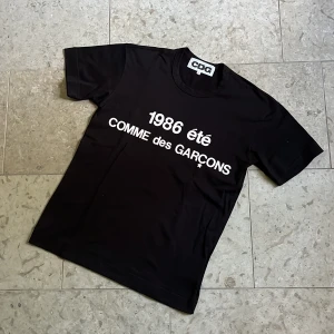 Svart Cdg t-shirt XS - Svart t-shirt från Cdg med vit text '1986 été' och logga på bröstet. Storlek S men passar som en XS, toppskick och fraktas inom 24h✅