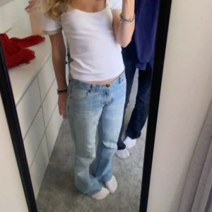 Ljusblå bootcut jeans  - Säljer ett par ljusblå jeans med bootcut passform. Jeansen har klassiska fem fickor, låg midja och är tillverkade i mjukt denim. Snyggt slitna detaljer och raka ben som går ut lite nertill för en retro vibe.