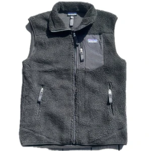 Svart fleeceväst från Patagonia - Mysig svart fleeceväst från Patagonia med hög krage och dragkedja framtill. Västen har två sidofickor med dragkedja och en bröstficka med logga. Perfekt för lager-på-lager och chill vardagsstil.