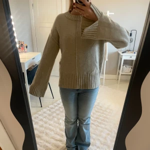 Beige stickad tröja från Vila - Beige stickad tröja från Vila med breda ribbade muddar vid ärmslut och nederkant. Tröjan har en rak passform, rund halsringning och diskret söm framtill. Perfekt för lager-på-lager och chill höst- eller vinterstil.