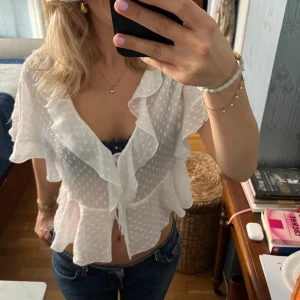 Vit volangblus från Zara - Supersöt vit blus från Zara med volanger och små prickar i tyget. Blusen är genomskinlig, har korta ärmar och knäpps framtill med tygklädda knappar. Perfekt för en fräsch och romantisk look.